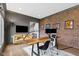 Comfortable home office featuring brick accent wall, hardwood floors, modern desk, and cozy seating area at 6590 W Deerfield Dr, Zionsville, IN 46077
