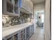 Butler pantry features grey cabinets, floral wallpaper, quartz counters, and glass door uppers at 15594 Garrano Ln, Fishers, IN 46040