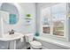 A powder room with a pedestal sink, rounded mirror, and ample natural light at 7501 Independence Dr, Zionsville, IN 46077