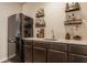 Wet bar with granite counter, dark cabinets, beverage cooler, and open shelving for storage at 5869 Belchamp Dr, Noblesville, IN 46062