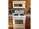Close up of a white oven range with overhead microwave and adjacent wooden cabinetry at 5210 S 100 E Rd, Anderson, IN 46013