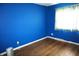 Bright blue bedroom with hardwood floors, a large window, and a corner view, showcasing a vibrant, modern space at 5363 Channing Rd, Indianapolis, IN 46226