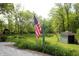 Well-maintained backyard featuring an American flag, small shed, landscaping, and lush greenery at 701 E Main St, Westfield, IN 46074