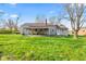 Back exterior view showcasing the home, large yard, covered patio, and mature trees at 7008 E Jackson St, Muncie, IN 47303