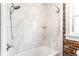 Updated shower and tub featuring marble style tile, modern shower head, and exposed brick accents at 801 N Pennsylvania St # Apt D, Indianapolis, IN 46204