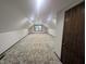 The attic has neutral walls, carpet, lighting, and a small window at the far end at 8017 Dogwood Ct, Plainfield, IN 46168