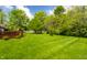 Expansive green backyard with a wooden deck, bordered by lush trees, and a clear blue sky at 9338 Eden Woods Ct, Indianapolis, IN 46260