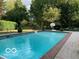Outdoor pool and brick patio area next to mature trees and landscaped backyard at 10605 Winterwood, Carmel, IN 46032