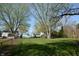 View of the backyard with mature trees, a trampoline, and buildings in the distance at 10360 Wilson Rd, Brownsburg, IN 46112