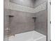 A modern shower with gray tile, white tub, mosaic details, and corner shelves at 8083 Easton Ln, Zionsville, IN 46077