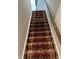 Carpeted staircase with a red and tan pattern and a wooden handrail at 1303 Eton Way, Avon, IN 46123