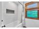 The bathtub features white tile surround, a rain shower head, and a window that provides natural light at 2011 Pin Oak Ct, Indianapolis, IN 46260