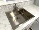 Close-up of a stainless steel kitchen sink set into marble countertop with a white backsplash at 410 S 25Th Ave, Beech Grove, IN 46107