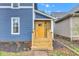 Inviting yellow front door with wooden steps, set against a blue-sided home and landscaped garden bed at 614 Park Ave, Anderson, IN 46012