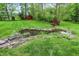 Picturesque backyard pond with rock border, lush plants, and a bridge surrounded by manicured lawn at 3875 Arrowhead Ct, Greenfield, IN 46140