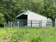 Exterior view of a metal Morton barn with a green metal roof and fenced enclosure surrounded by lush trees and field at 685 N Buffalo Hill Rd, Martinsville, IN 46151