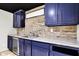 Wet bar boasts blue cabinets, granite counters, stone backsplash, and a wine fridge at 10715 Hamilton Pass, Fishers, IN 46037