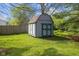 Outdoor shed with double doors sits on green lawn in backyard with wooden fence and landscaping at 7104 Combs Rd, Indianapolis, IN 46237