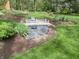 Charming backyard landscape featuring a decorative wooden bridge, river rock, mature shade trees, and meticulously maintained grass at 10561 Wilson Rd, Brownsburg, IN 46112