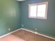 A simple bedroom with a green wall, window, and worn-out flooring at 1221 S Catherwood Ave, Indianapolis, IN 46203