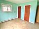 A simple bedroom with a blue wall, window, two doors, and worn-out flooring at 1221 S Catherwood Ave, Indianapolis, IN 46203