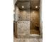 Walk-in shower showcasing custom earth-tone tile work, frameless glass enclosure, built-in seat, and sleek showerhead at 12715 Norfolk Ln, Carmel, IN 46032