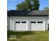 View of the detached two-car garage with white doors and siding, complemented by a dark roof and lush green lawn at 1802 Poplar St, Anderson, IN 46012