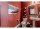 Cozy powder room with pedestal sink, decorative mirror, artwork and red accent wall at 16080 Cabin Hill Dr, Noblesville, IN 46060