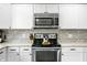 Close up of kitchen appliances, including stainless steel oven and microwave, with granite countertops and white cabinets at 3615 Dawnwood Dr, Indianapolis, IN 46227