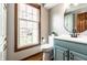 Charming bathroom featuring a wood-framed window, blue vanity, and modern round mirror at 8142 Bittern Ln, Indianapolis, IN 46256