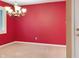 Empty dining room boasts a modern chandelier, neutral carpet, and red accent wall at 11 Woodacre Dr, Carmel, IN 46032