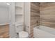 Bright bathroom featuring wood-look tiling in shower/tub and convenient built-in shelving next to toilet at 1627 Lawton Ave, Indianapolis, IN 46203
