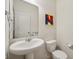 Charming powder room featuring a pedestal sink, toilet, decorative mirror, and a colorful art piece at 8855 Banner Dr, Brownsburg, IN 46112