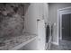 Modern laundry room with side-by-side washer and dryer, stone countertop, unique stone accent wall, and cabinets at 5925 Silas Moffitt Way, Carmel, IN 46033