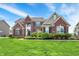 Beautiful two-story brick home featuring a well-manicured lawn and lush landscaping, set against a bright, blue sky at 13728 Oliver Ln, Carmel, IN 46074