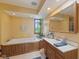 Bright bathroom with wood-paneled tub, double sink vanity, and natural light from a window with green plants at 10220 N Serenity Ln, Mooresville, IN 46158