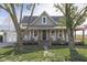 Charming green farmhouse with covered front porch and rocking chairs surrounded by mature trees at 10776 S 250 W, Flat Rock, IN 47234