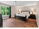 Main bedroom featuring hardwood floors, a dark wood bed frame, and a side view of lush landscaping at 2450 S Us 421, Zionsville, IN 46077
