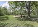 Large backyard showing grass, mature trees, wood firepit, and four lawn chairs at 1301 Stafford Rd, Plainfield, IN 46168