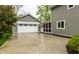 View of the two-car garage with white carriage doors and lush landscaping around a gray two story home at 440 E 82Nd St, Indianapolis, IN 46240