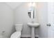 Neat half bath with white pedestal sink, oval mirror, and a toilet; painted in a clean, neutral gray at 13776 Tender Dr, Carmel, IN 46032