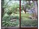 View of the backyard through a window, showcasing lush landscaping and a small shed at 8728 Holliday Dr, Indianapolis, IN 46260