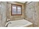 Comfortable bathtub with travertine tile surround and a window for natural light at 621 Thorne Dr, Brownsburg, IN 46112