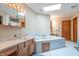 Bathroom featuring a large tiled whirlpool tub, double vanity with marble countertops, and a skylight at 6212 Rocklane Rd, Greenwood, IN 46143