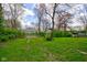 Lush green backyard view features trees surrounding a white sided house with a grassy lawn at 1467 W 33Rd St, Indianapolis, IN 46208