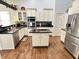 Kitchen with white cabinetry, black countertops, stainless steel appliances, and hardwood flooring at 18680 Long Walk Ln, Noblesville, IN 46060