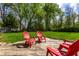 A wooden deck with red Adirondack chairs overlooking a spacious yard with lush green grass and mature trees at 7423 Scarborough Blvd E Dr, Indianapolis, IN 46256