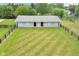 Aerial view of a horse barn, set within a black fence perimeter and a generous green pasture at 14655 Little Eagle Creek Ave, Zionsville, IN 46077