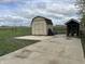 A shed with a gray door and brown roof sits on a concrete slab surrounded by a green lawn at 5282 W Blue Bell Dr, New Palestine, IN 46163