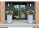 Close-up of the front door, flanked by large planters with flowers and elegant sconces lighting the entryway at 11064 Hamilton Run, Zionsville, IN 46077
